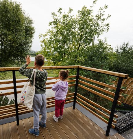 Brother with sister stand on wooden terrace of modern wood stone Brother with sister stand on wooden terrace of modern wood stone house.